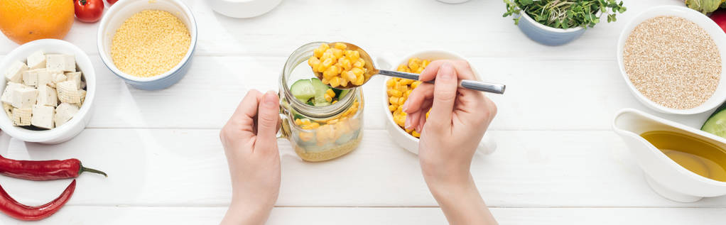 cropped view of woman adding corn in jar with salad on wooden white table, panoramic shot - Photo, Image