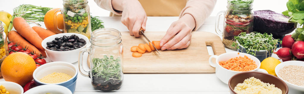 cropped view of woman in apron cutting carrots on wooden table isolated on white, panoramic shot - Photo, Image