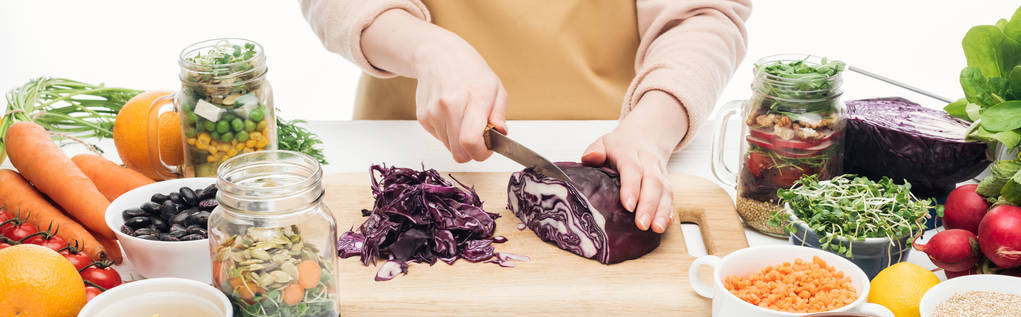 cropped view of woman in apron cutting red cabbage on wooden table isolated on white, panoramic shot - Photo, Image