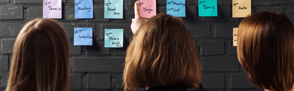visão traseira de mulheres apontando com o dedo para a parede de tijolo preto, mostrando almofadas adesivas coloridas com notas sobre
  - Foto, Imagem