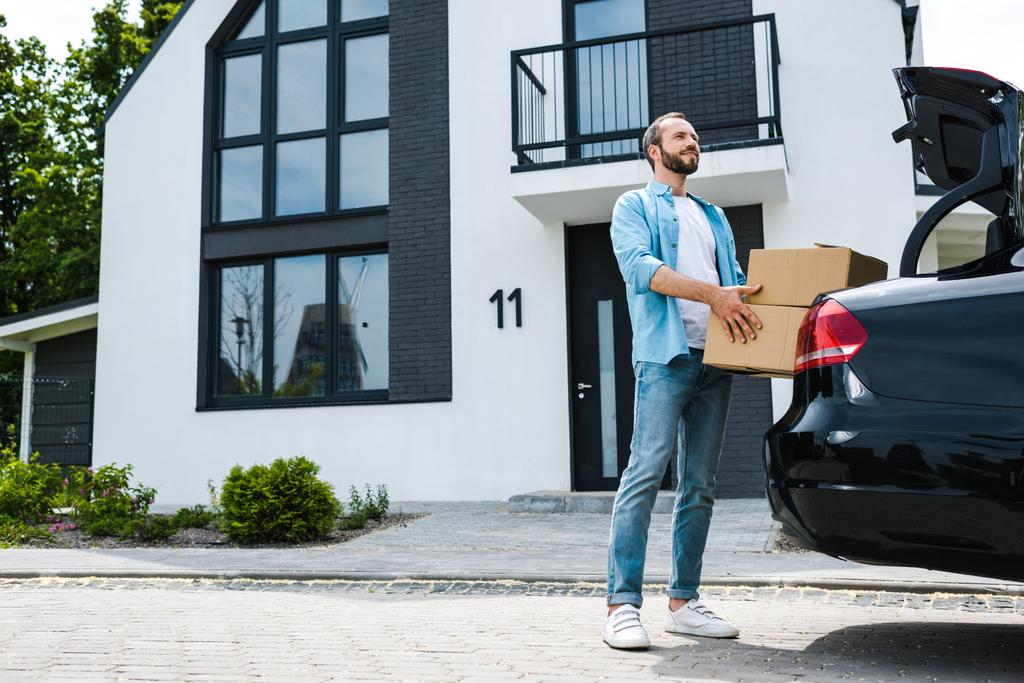 счастливый человек, держащий коробки возле машины и современного дома
  - Фото, изображение