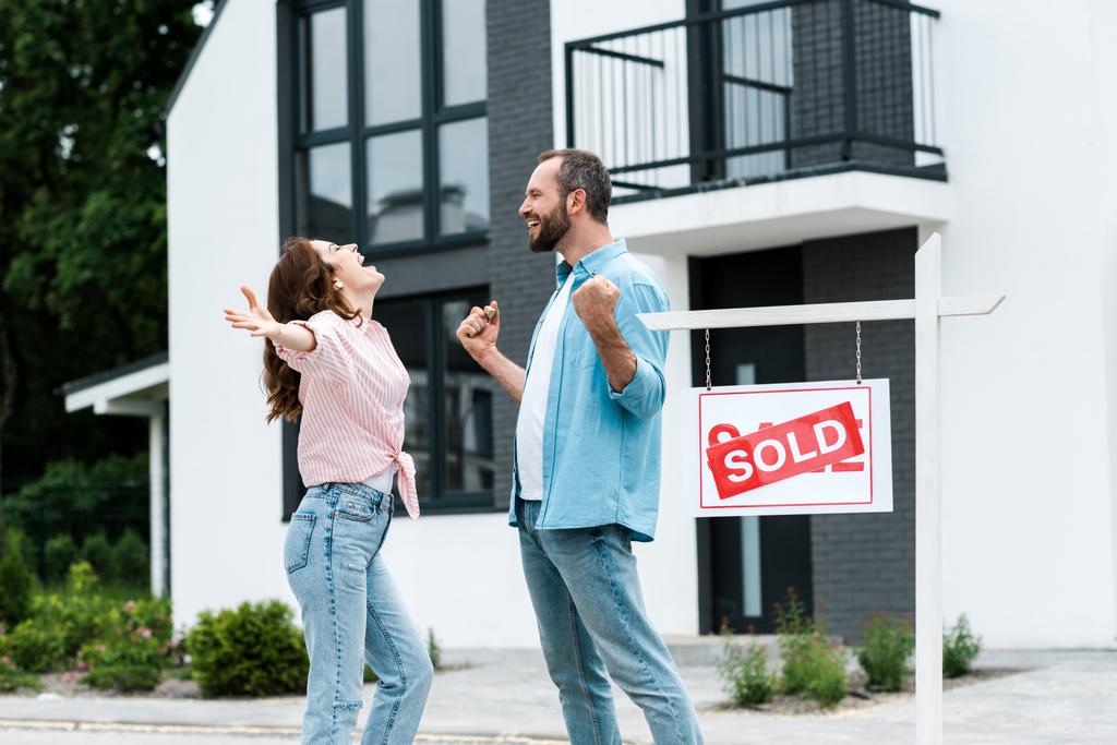 happy man and woman celebrating near house and board with sold letters  - Photo, Image