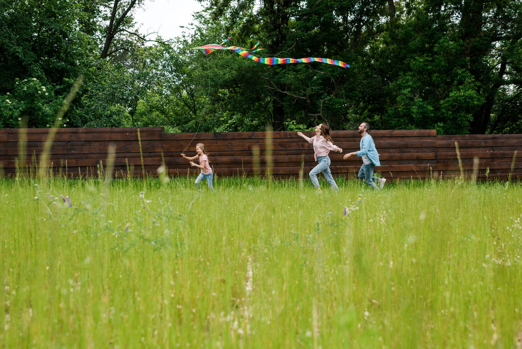 Selektiver Fokus des niedlichen Kinderlaufs mit buntem Drachen in der Nähe der Eltern  - Foto, Bild
