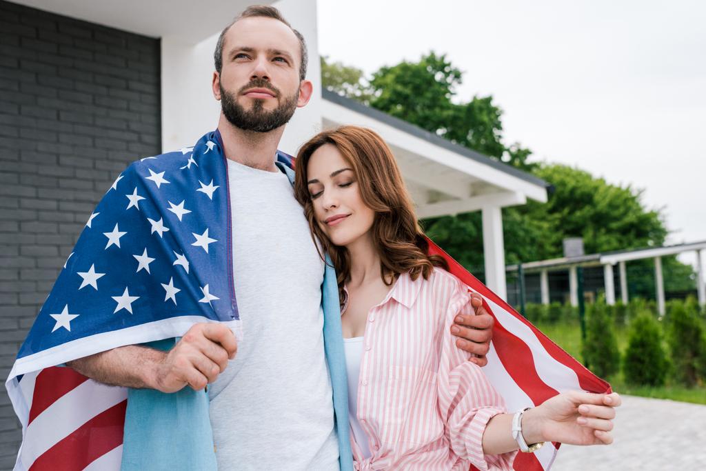 アメリカの旗を持ち、ハンサムな男と立っている目を閉じた魅力的な女性  - 写真・画像