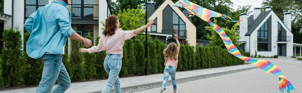tiro panorâmico de criança correndo com pipa colorida perto de pais na rua
  - Foto, Imagem