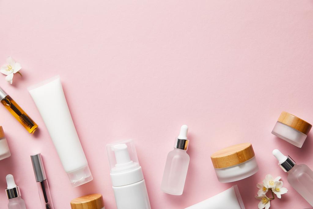 bovenaanzicht van crèmekleurige buizen, cosmetische dispenser, lege potten en met handcrème, mascara flessen op roze  - Foto, afbeelding