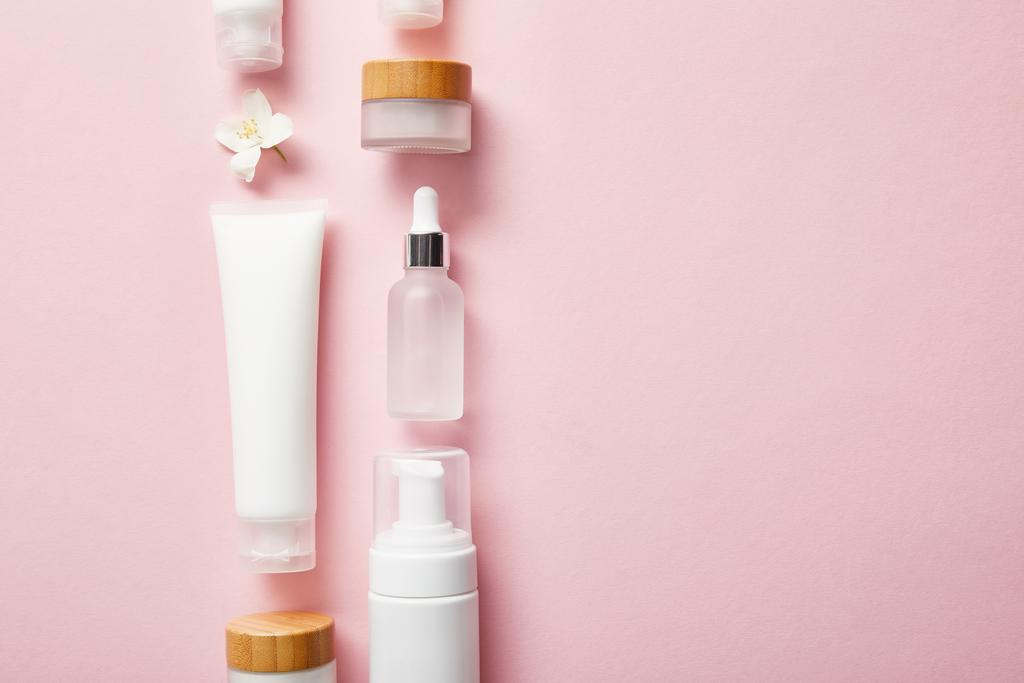 flache Lage verschiedener Kosmetikbehälter und Jasminblüte auf rosa  - Foto, Bild