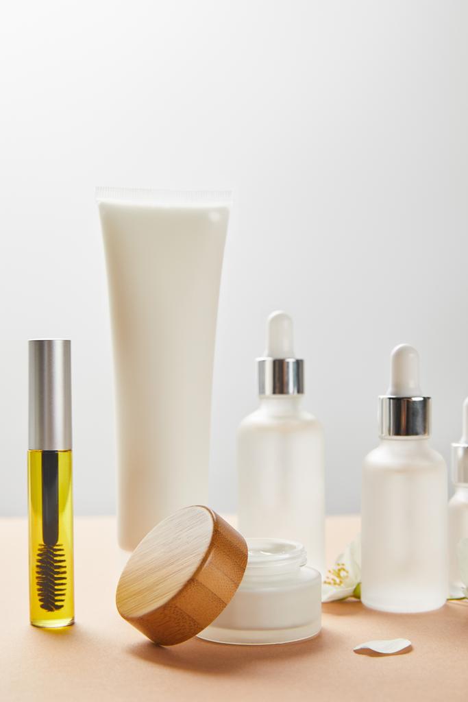 mascara bottle with natural oil, cream tube, cosmetic glass bottles, open jar with wooden cap and jasmine flower on beige  - Photo, Image