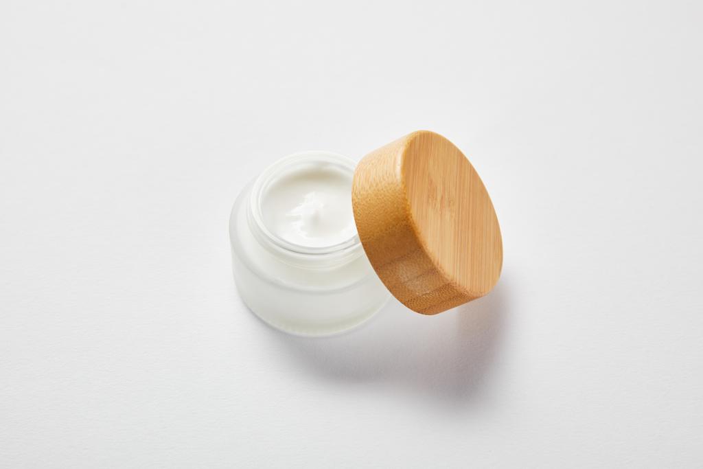 pot en verre ouvert avec crème et capuchon en bois sur blanc
  - Photo, image