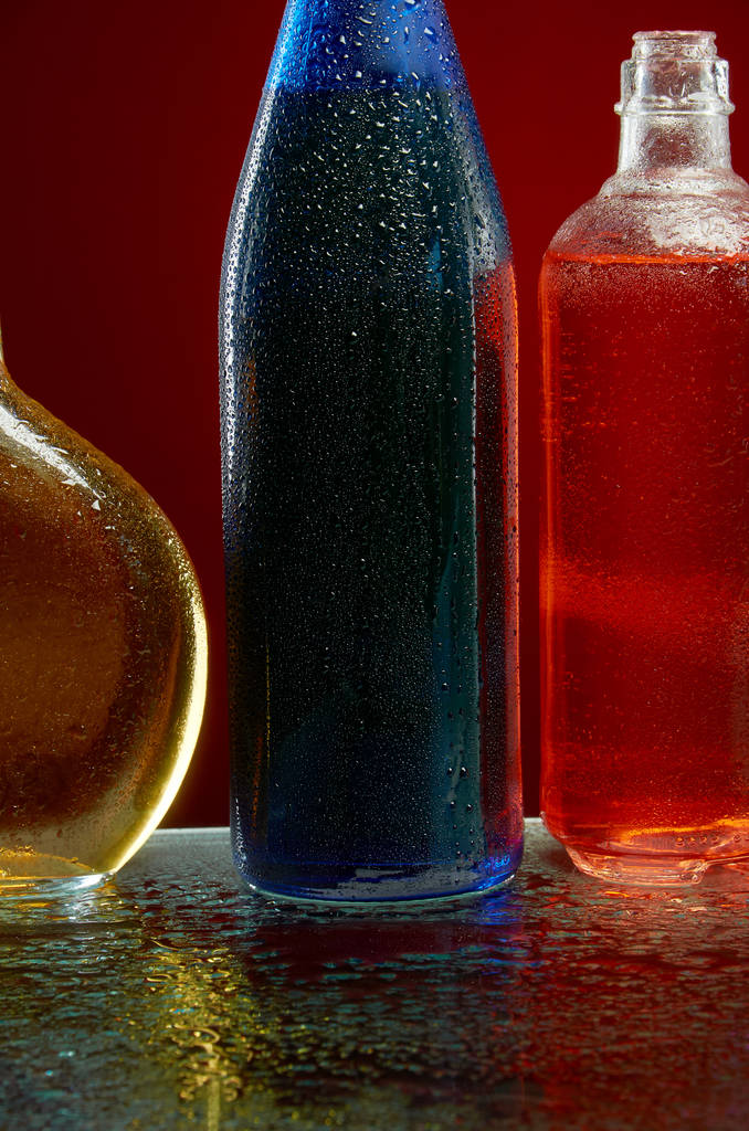 Alcohol flessen in water druppels op rode achtergrond - Foto, afbeelding