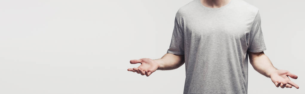 bijgesneden weergave van de mens in grijs t-shirt met schouderophalend gebaar geïsoleerd op grijs, panoramisch schot, menselijke emotie en expressie concept - Foto, afbeelding