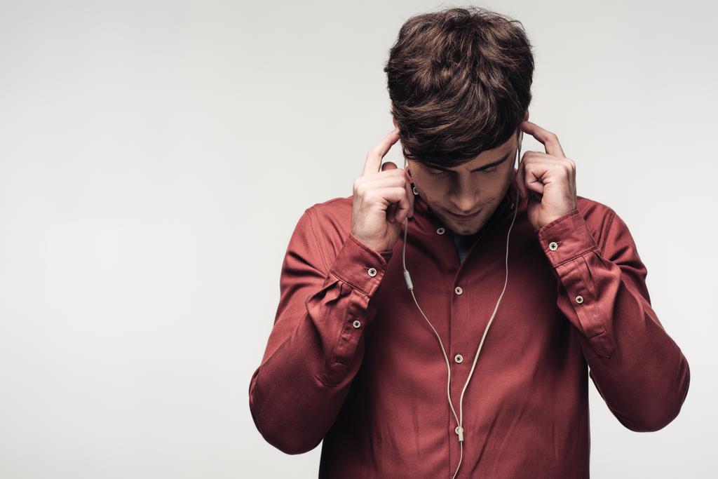 νέος άνδρας ακούγοντας μουσική σε ακουστικά με κυρτό κεφάλι απομονωμένο σε γκρι - Φωτογραφία, εικόνα