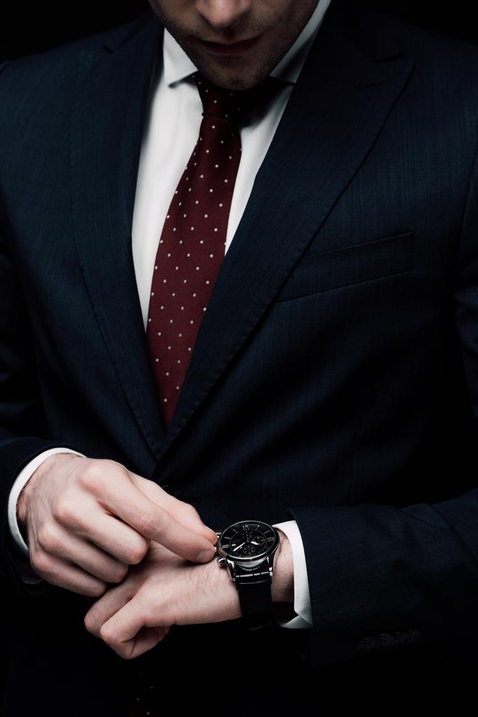 abgeschnittene Ansicht eines Geschäftsmannes, der die Uhrzeit auf der Uhr kontrolliert, isoliert auf schwarz - Foto, Bild