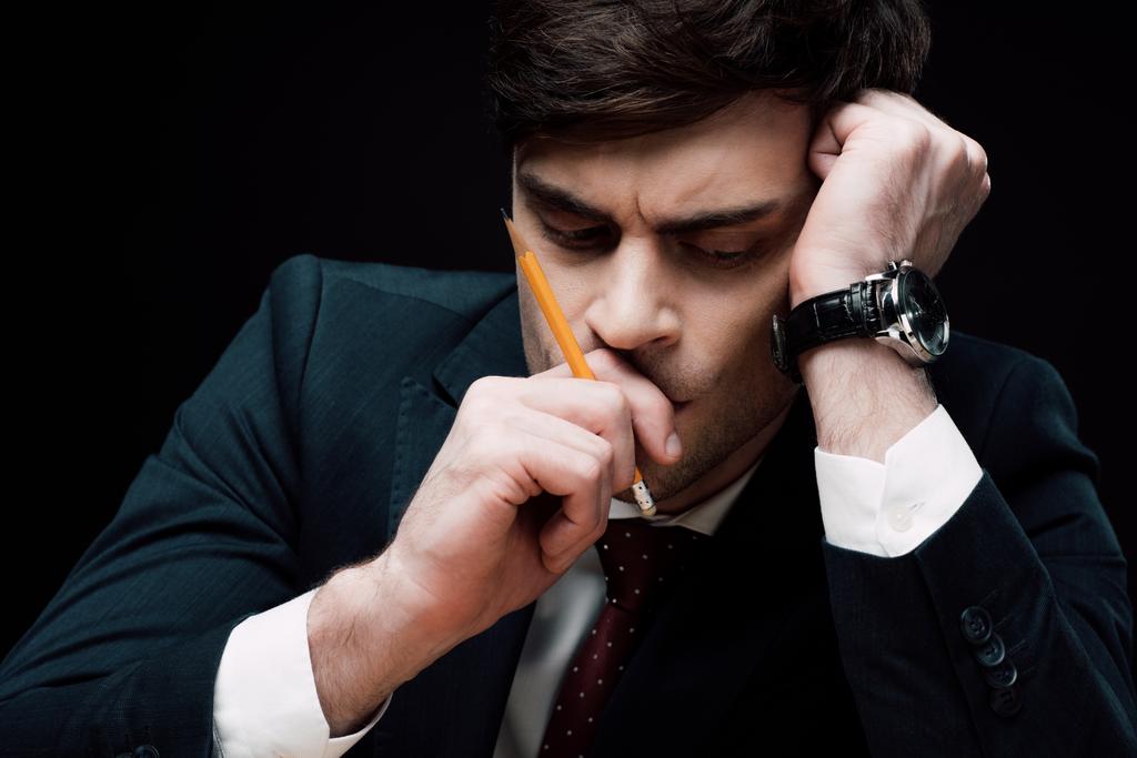 расстроенный, вдумчивый бизнесмен держит за руку карандаш рядом с лицом изолированным от черного
 - Фото, изображение