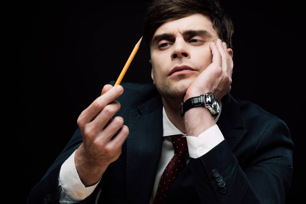 στοχαστικός επιχειρηματίας κοιτάζοντας το μολύβι στο χέρι απομονώνεται σε μαύρο - Φωτογραφία, εικόνα