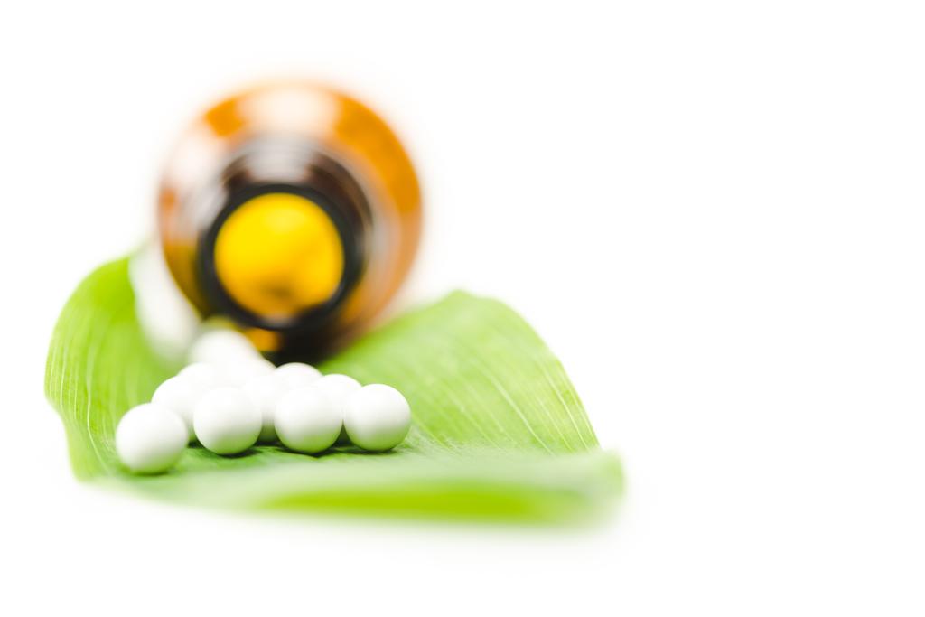 szelektív középpontjában a kis kerek tabletták zöld levél közelében palack izolált fehér  - Fotó, kép
