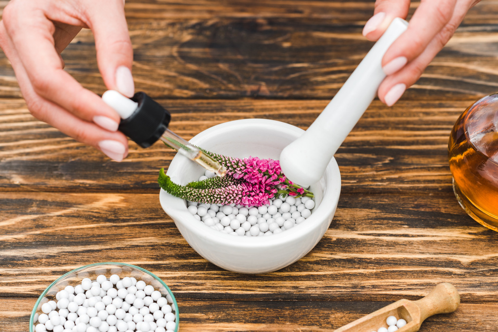cropped view of woman holding pestle and pipette near mortar with veronica flowers and pills on wooden table  - Photo, Image