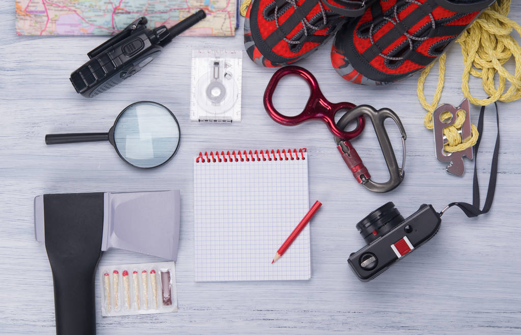 on a light background, a set for the traveler, ax, compass, rope, carabiner, magnifying glass, comfortable shoes, walkie-talkie, matches, camera ,map and notebook with pencil for records - Photo, Image