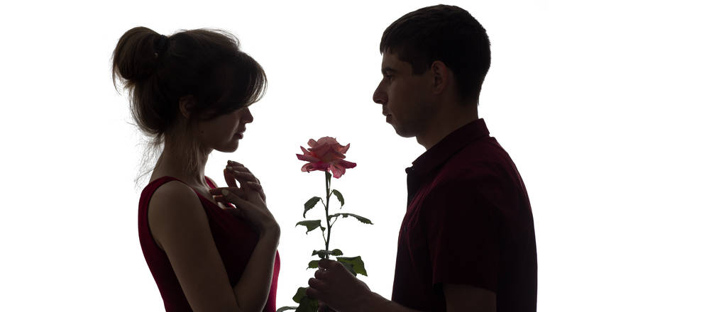 προφίλ σιλουέτας από ένα νεαρό ζευγάρι στην αγάπη σε λευκό απομονωμένο υπόβαθρο, ο άνθρωπος δίνοντας σε μια γυναίκα ένα τριαντάφυλλο λουλούδι, concept αγάπη και ρομάντζο - Φωτογραφία, εικόνα