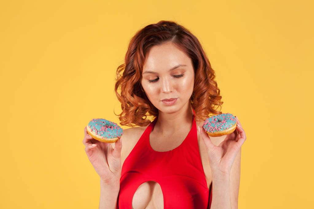 дівчина в червоному купальнику тримає пончики з блакитною глазур'ю на жовтому фоні
 - Фото, зображення