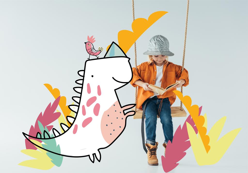 cute kid in jeans and orange shirt sitting on swing and reading book on grey background with fantasy bird and dinosaur illustration - Photo, Image