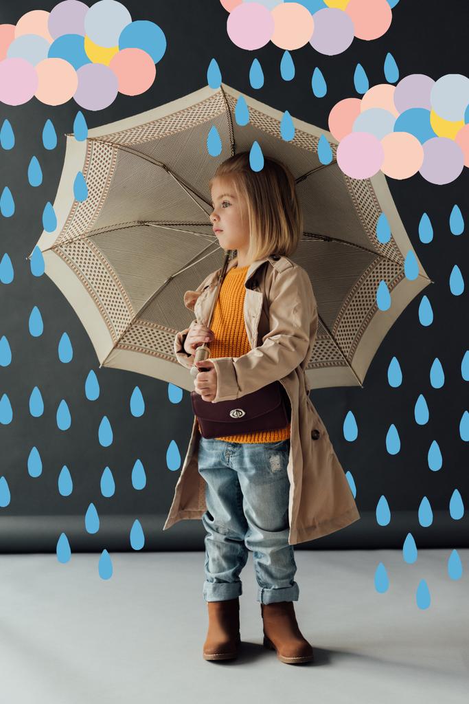 トレンチコートとジーンズを着た深刻な子供は、妖精の雨の下で傘を持ち、目をそらす  - 写真・画像