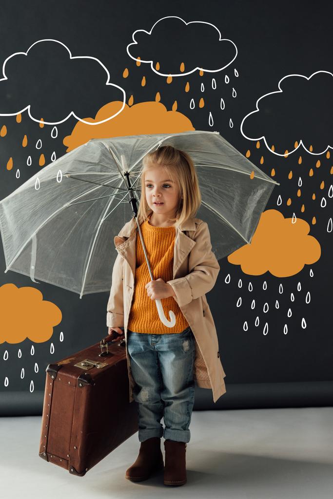 child in trench coat and jeans holding umbrella and leather suitcase under fantasy rain on black background - Photo, Image