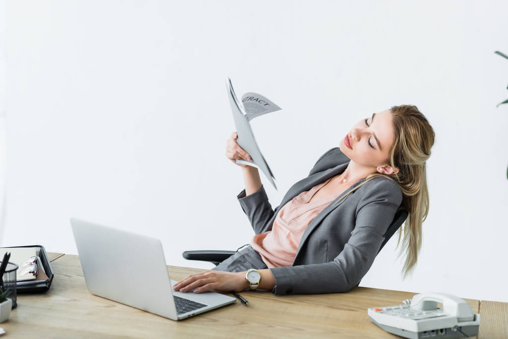 бізнес-леді, сидячи в офісі, тримає папку в руці, працює на ноутбуці і страждає від спеки
 - Фото, зображення