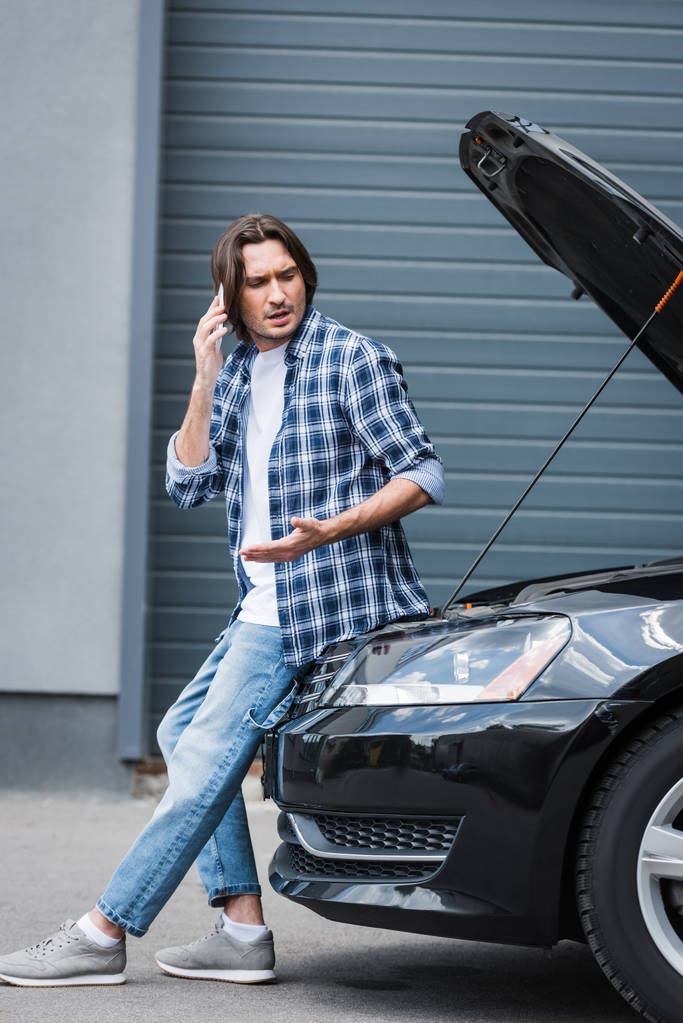 man praat op smartphone in de buurt van Broken auto met open trunk, autoverzekering concept - Foto, afbeelding