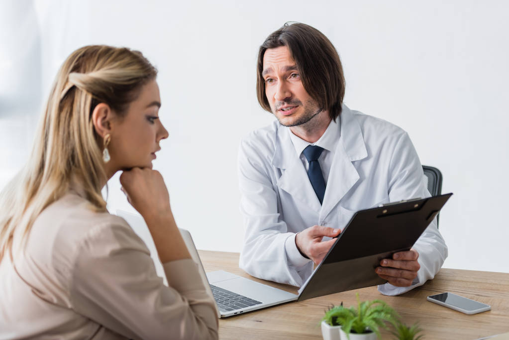 beau médecin tenant le document dans les mains, regardant le patient et assis derrière la table en bois
 - Photo, image