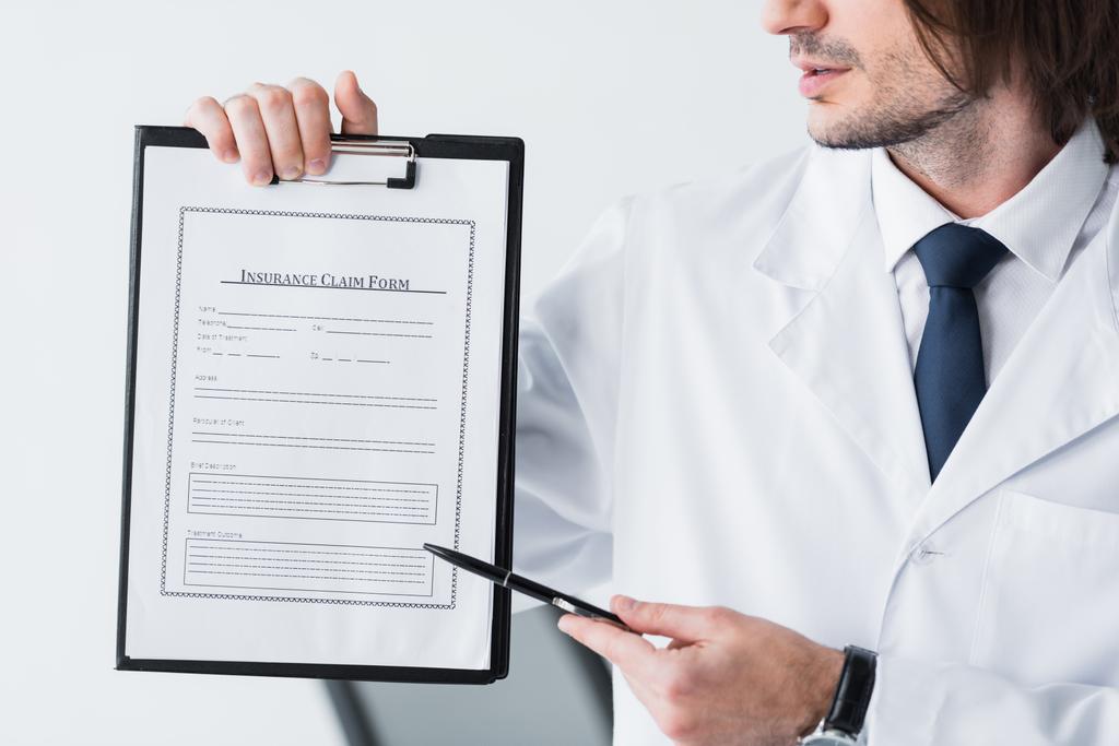 医療文書でペンを指す白いコートを着た医師のトリミングされたビュー  - 写真・画像