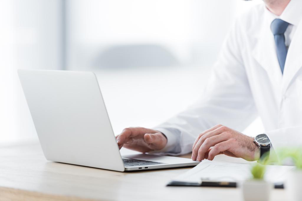 vista recortada del médico en bata blanca trabajando con el ordenador portátil
 - Foto, imagen