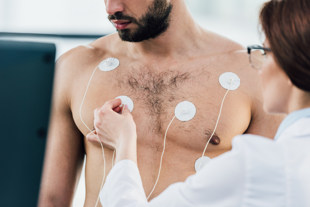 Ausgeschnittene Ansicht eines Arztes, der beim Härtetest Elektroden am hemdslosen Sportler anlegt - Foto, Bild