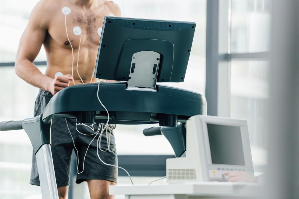selektywne skupienie sportowca z elektrodami biegnący na bieżni podczas testu wytrzymałościowego w siłowni - Zdjęcie, obraz