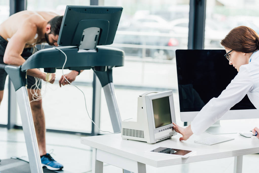 Arzt schaut beim Härtetest mit Sportler im Fitnessstudio auf Monitor - Foto, Bild