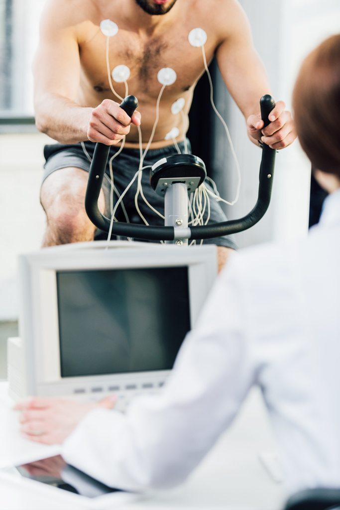 περικομμένη άποψη του γιατρού που διεξάγει δοκιμή αντοχής με αθλητή με ηλεκτρόδια στο γυμναστήριο - Φωτογραφία, εικόνα