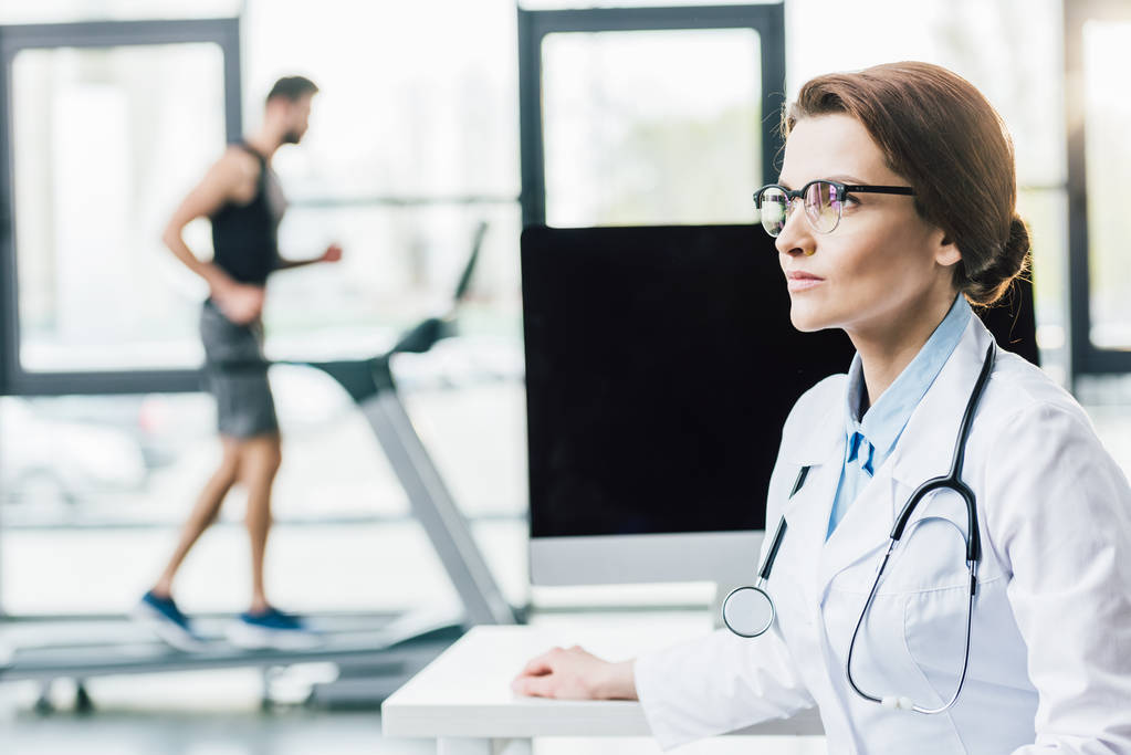 selective focus of doctor near sportsman running on treadmill during endurance test in gym - Photo, Image