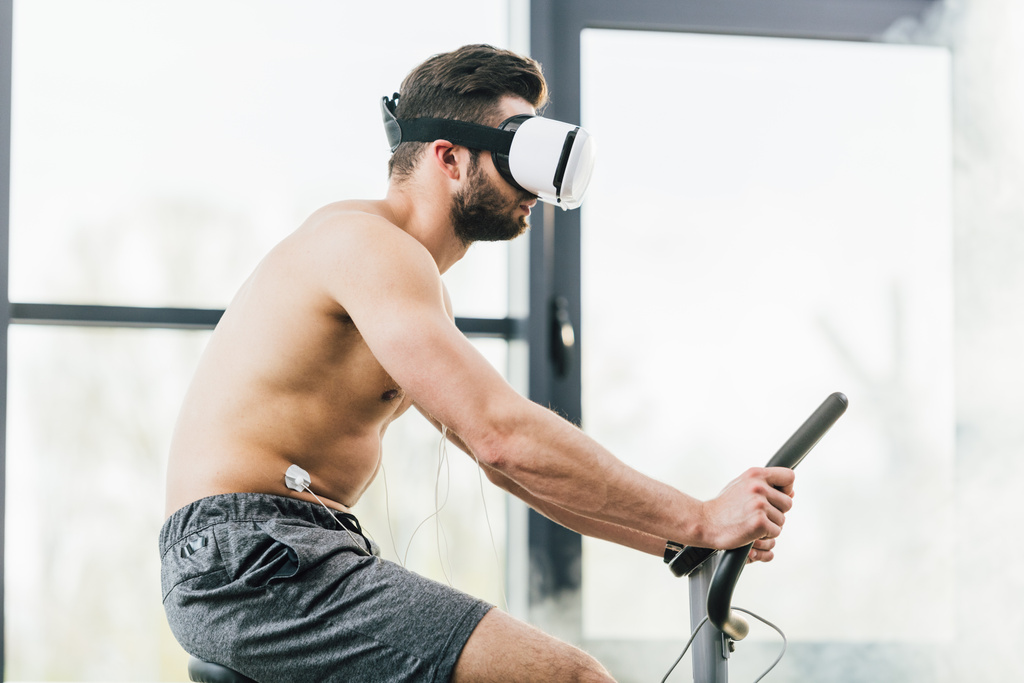 shirtless sportman in Virtual Reality headset met elektroden training op elliptische tijdens uithoudingsvermogen test in de sportschool - Foto, afbeelding