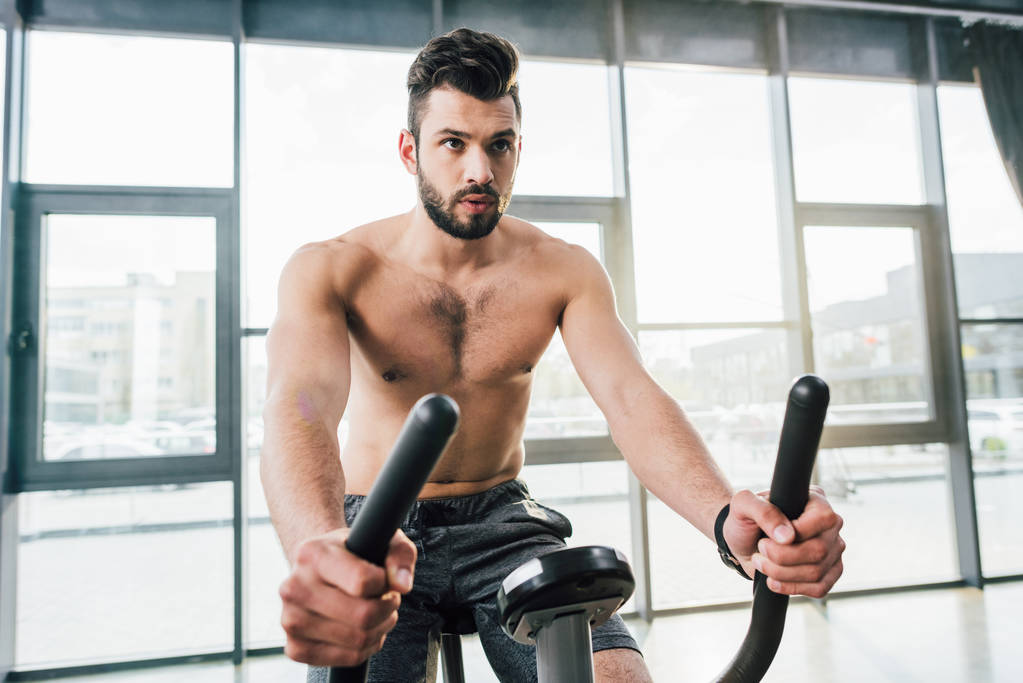 handsome shirtless sportsman training on elliptical machine at gym - Photo, Image