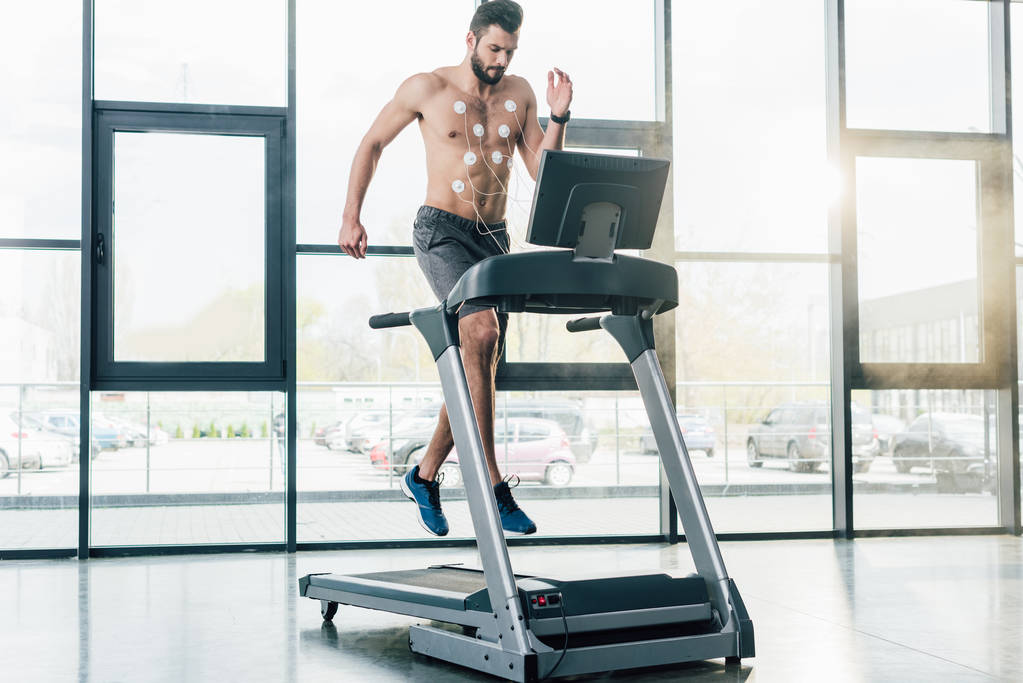 przystojny sportowiec z elektrodami biegowymi na bieżni podczas testu wytrzymałościowego w siłowni - Zdjęcie, obraz