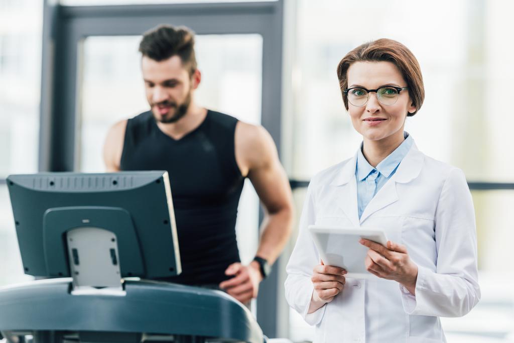 Sportler läuft beim Härtetest im Fitnessstudio neben attraktivem Arzt auf Laufband - Foto, Bild