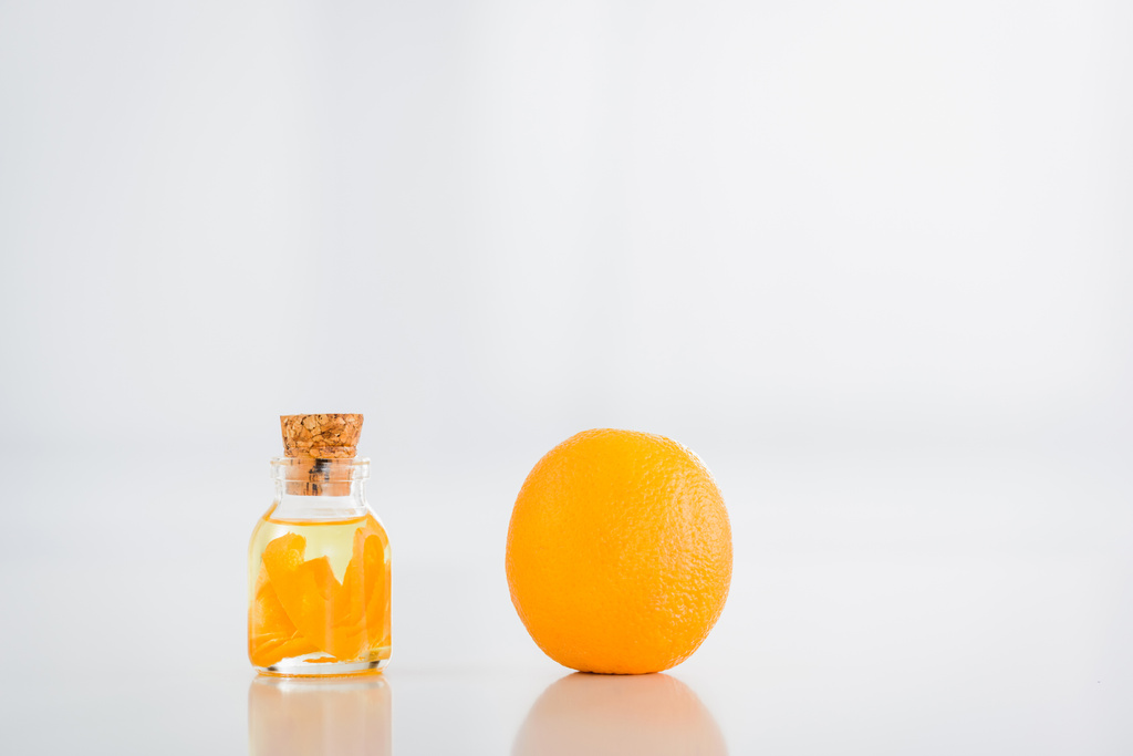 целый оранжевый рядом пробки стеклянная бутылка с эфирным маслом на белом фоне
 - Фото, изображение