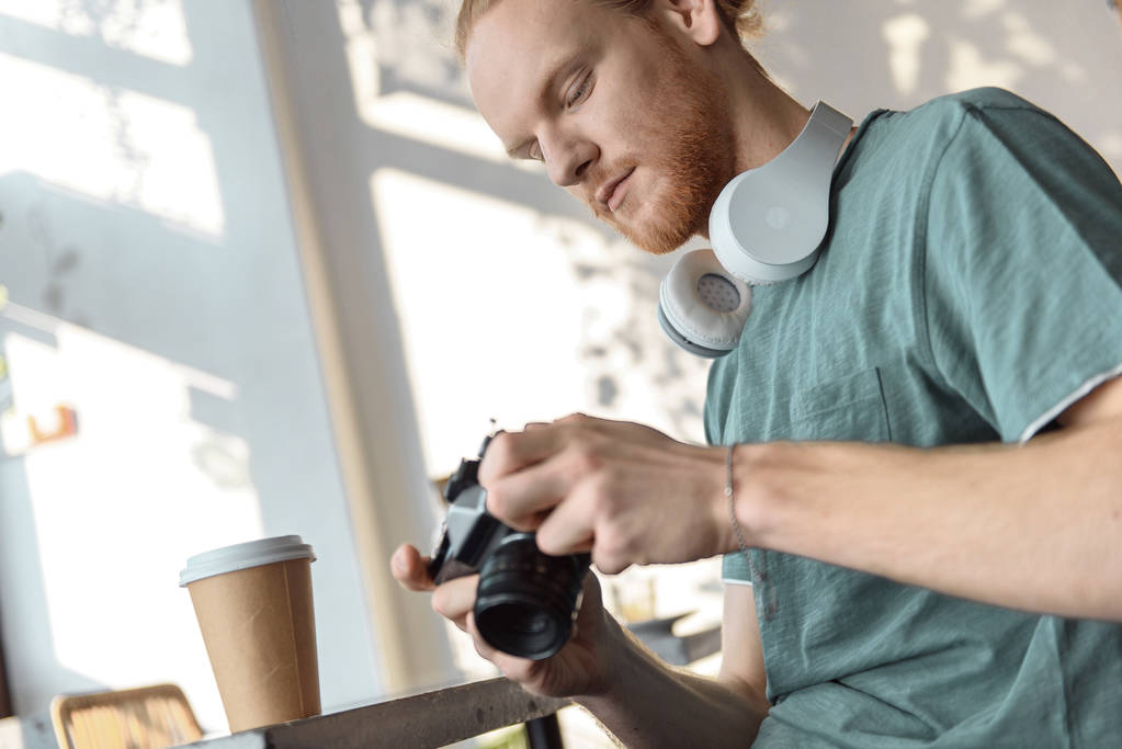 Młody mężczyzna używa retro kamery w kawiarni - Zdjęcie, obraz