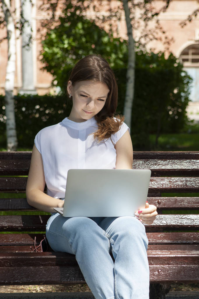 beautiful young student girl sitting on a bench with a laptop an - Photo, Image