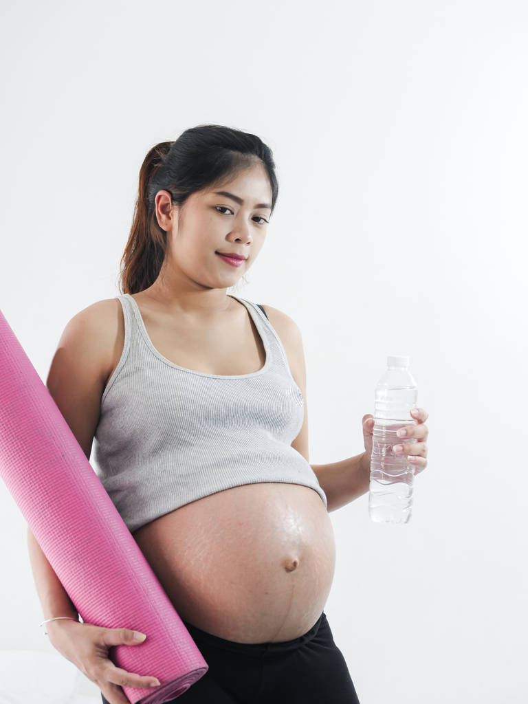asiatische schwangere Frau hält rosa Yogamatte und eine Flasche Wasser - Foto, Bild