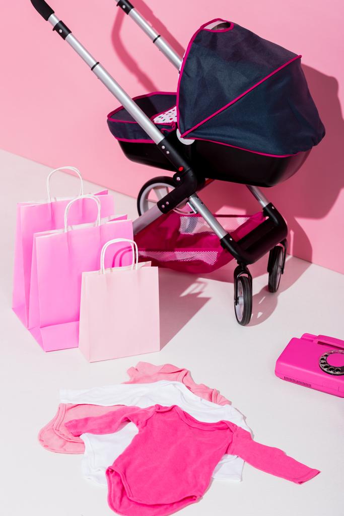 carrito de bebé, bolsas de compras, trajes corporales y teléfono en rosa
 - Foto, imagen