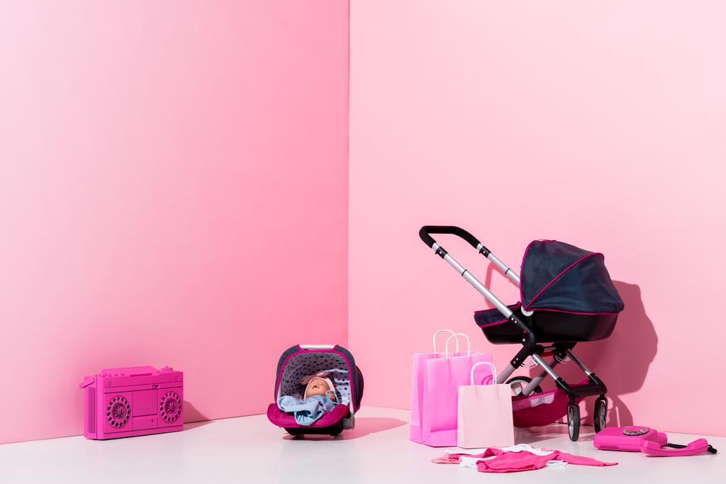 Kinderwagen, Puppe im Tragetuch, Einkaufstaschen und Boombox auf rosa - Foto, Bild