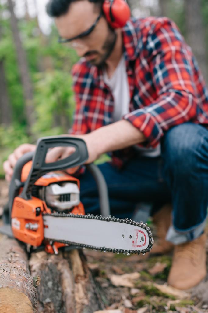 selective focus of lumberjack repairing electric chainsaw in forest - Photo, Image