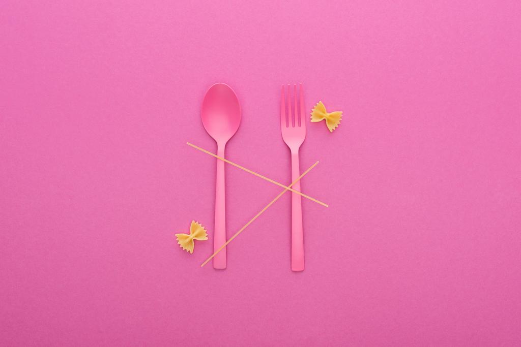 Różowa plastikowa łyżka i widelec, spaghetti i dwa niegotowane makarony Farfalle izolowane na różowym - Zdjęcie, obraz