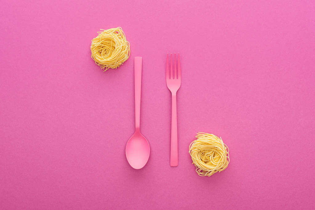 růžová plastová vidlička a lžíce vzhůru nohama blízko rýže těstoviny na růžovém pozadí - Fotografie, Obrázek